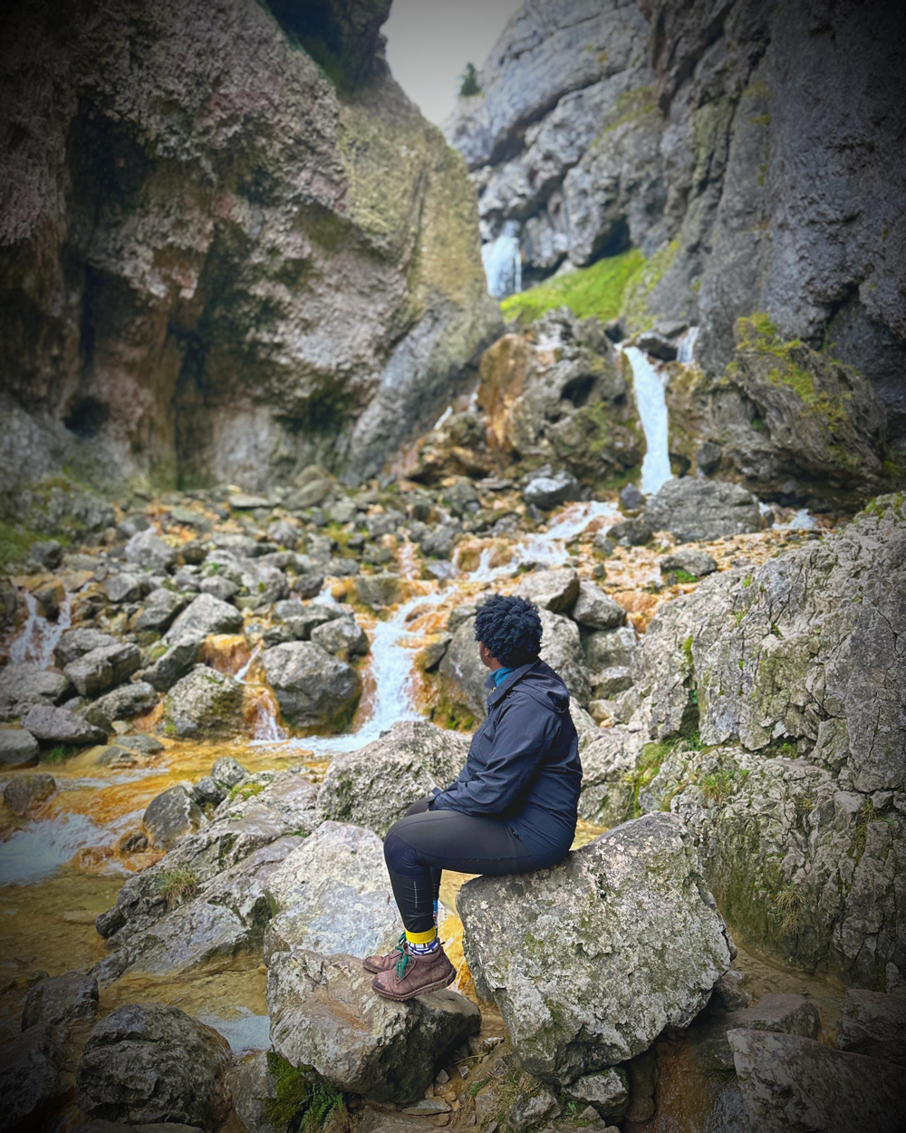Person sitting on rocks looking at a rocky stream and small waterfall in a steep gorge